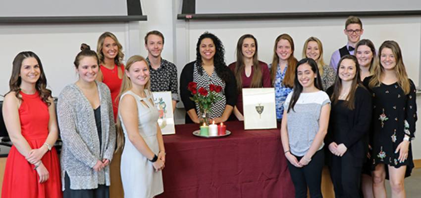 A group of Tri-Beta inductees standing by a table with flowers and candles